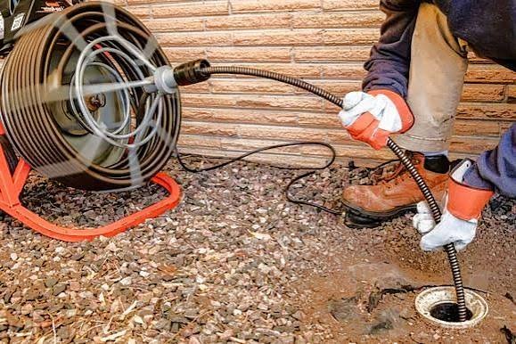 Electric motorized rooter snake machine feeding heavy-duty cable into outdoor drain cleanout
